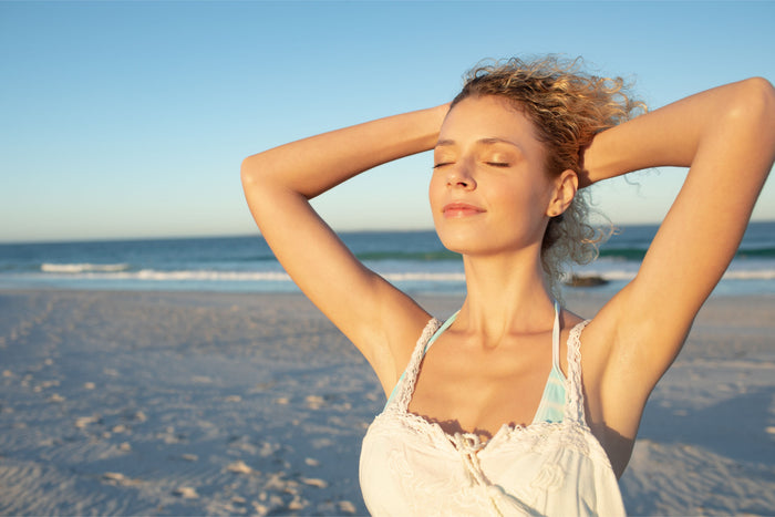 Femme au teint lumineux profitant du soleil sur la plage, illustrant les effets du photo-vieillissement sur la peau