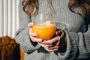Main tenant un grand verre de jus orangé à la lumière d’automne, symbole de vitalité, d’énergie et de bien-être naturel selon Vitamoon.