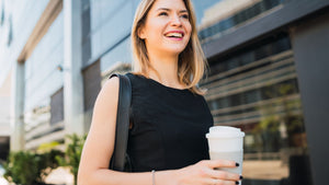 Femme active souriante tenant un café à emporter en marchant vers son bureau, symbole de la rentrée