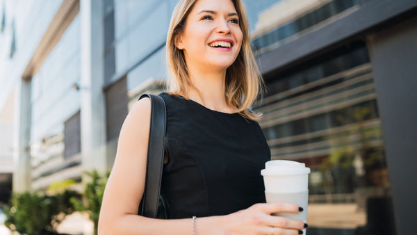 Femme active souriante tenant un café à emporter en marchant vers son bureau, symbole de la rentrée