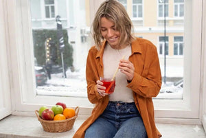Femme souriante buvant son collagène marin liquide aux fruits rouges Vitamoon lors d'un rituel bien-être matinal en hiver.