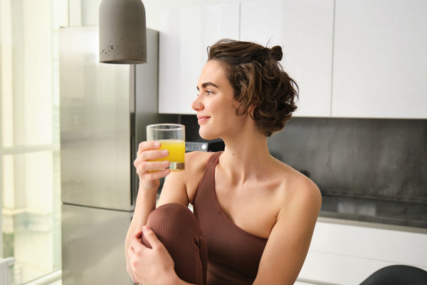 Femme souriante buvant un verre de jus d'orange le matin dans sa cuisine
