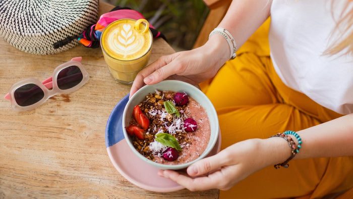 Femme dégustant un bowl de fruits rouges et granola accompagné d'un latte, moment de pause bien-être pour préparer son immunité à la rentrée