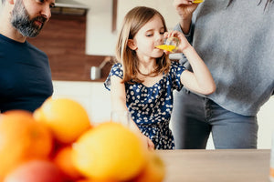 Jeune fille buvant la Multivitamine Liquide Vitamoon à table avec ses parents, montrant une consommation familiale associée à la vitalité et à l’énergie.